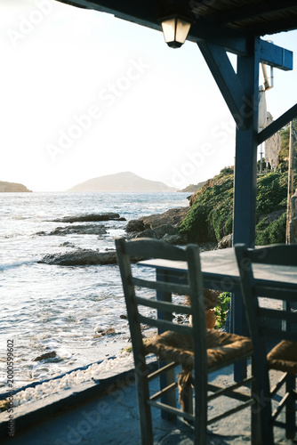 Seaside taverna with chairs and tables overlooking the ocean and distant island