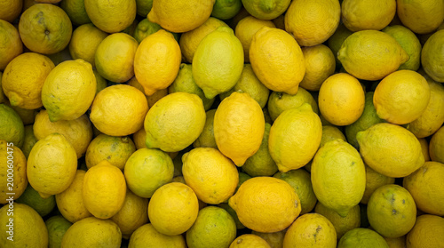 Fotografía ​A vibrant top-down view of a dense pile of fresh lemons, displaying various shades of bright yellow and lime green with textured skins, perfect for backgrounds