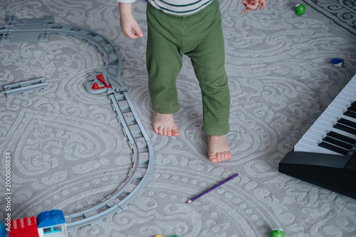 Feet of child walking on carpet next to toy train set and keyboard, kids playroom and creative development