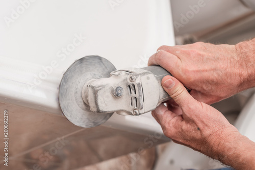 Closeup photo of man polishing bath tub surface with special tool. Worker polishing bathtub bottom with power grinder tool
