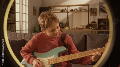 Front view of Caucasian young boy playing electric guitar and recording video for social media, shot framed with ring light lamp with copy space Great for personal branding or creator services