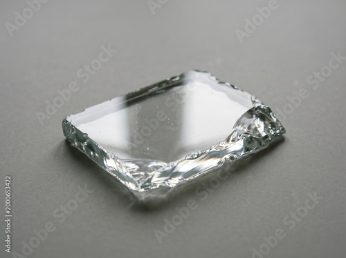 Small jagged glass shard slab with rough fractured edges on neutral gray surface for product background and material detail