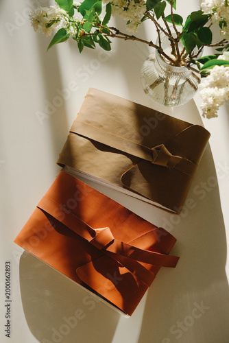 Two wrapped gift boxes with ribbon on a sunlit table, brown and orange tones, with flowers, creating a warm decor for celebration, present moments and gifting
