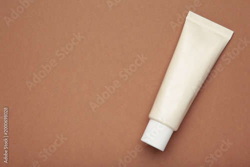 Beige tube of cream on brown background. Mockup plastic tube for cosmetics. Space for text