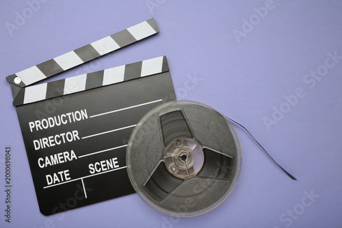 Movie clapper with popcorn and film reels on purple background. Space for text