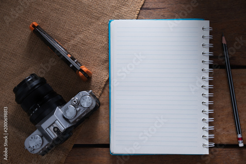Creative workspace with camera, blank notebook, and utility knife on wooden background.