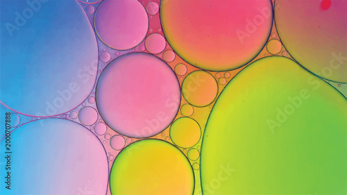 Vibrant macro of colorful oil droplets floating in water, featuring a spectrum of bright pink, blue, yellow, and green circular shapes of different sizes against a soft, glowing backdrop