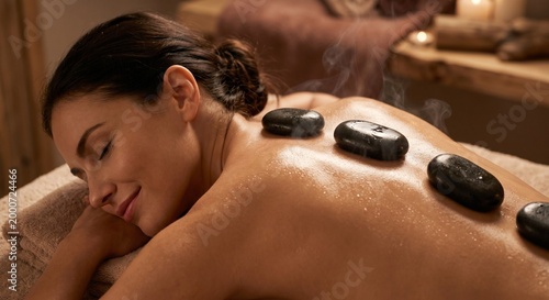 Close-up of a relaxed woman receiving a hot stone massage with visible steam and body oil, luxury spa wellness treatment.