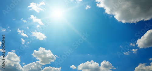 Clear blue sky with white fluffy clouds and bright radiant sun.