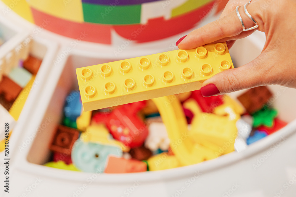 Fototapeta premium 19 October 2025, Belgrade, Serbia: Hand holding a yellow plastic toy block, ready for creative building