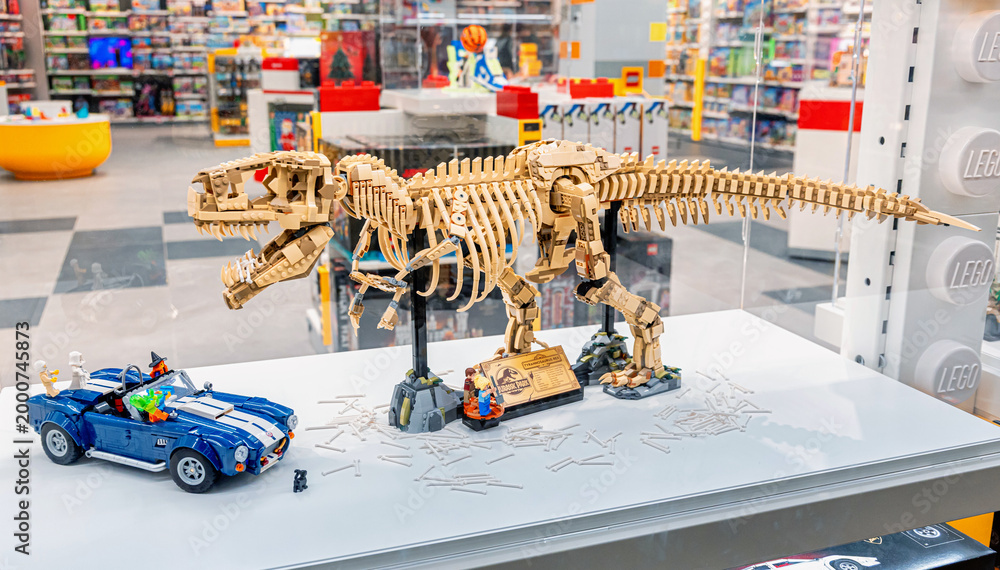 Naklejka premium 19 October 2025, Belgrade, Serbia: LEGO Tyrannosaurus Rex skeleton model displayed with a blue car in a bright modern toy store, showcasing popular brick built toys