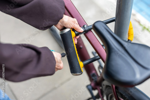 Senior Woman Securing Bicycle with U-Lock on City Street, close-up
 