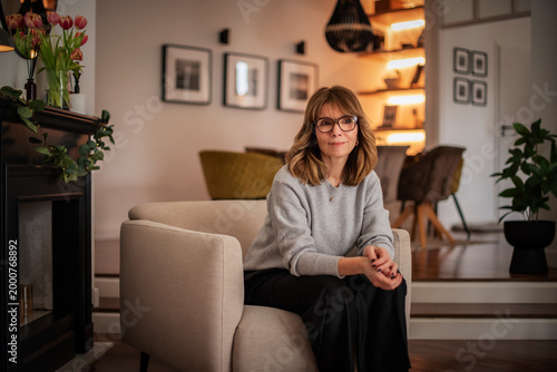 Blond haired attractive woman relaxing in an armchair in her modern apartment