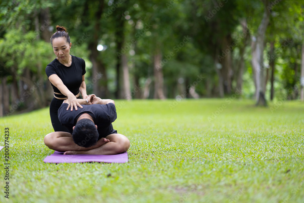 Naklejka premium People practicing outdoor yoga in a park guided by instructor, focusing on stretching and wellness while an instructor provides personal guidance to participant.