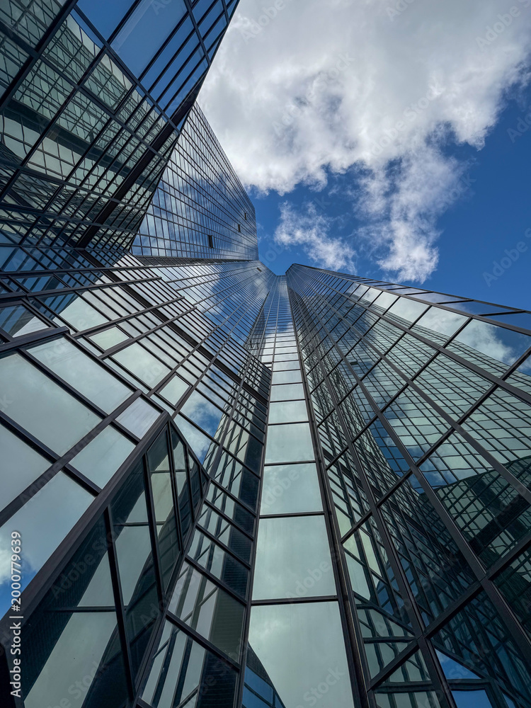 Obraz premium Glass skyscraper reflecting white clouds in blue sky.