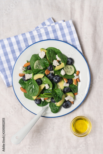 Healthy summer salad with avocado, spinach, almonds, cucumber, blueberries and feta cheese on linen tablecloth