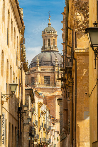 Narrow historic street in Salamanca leading to the majestic dome of La Clerecia church. A beautiful perspective of Spanish Baroque architecture and golden sandstone buildings in Spain
