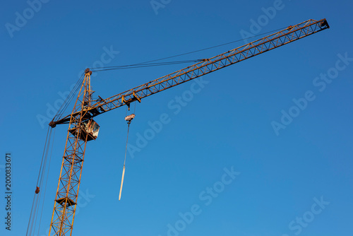 Construction tower crane with long boom on bright blue sky background.