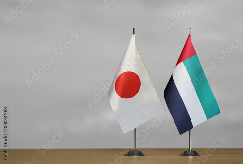 Two table flags of the Japan and Emirates on a blurred gray background