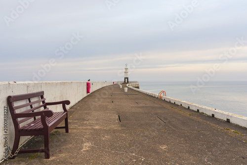 Принти на полотні A bench on the North Pier and the lighthouse in the background, Ramsey, Isle of
