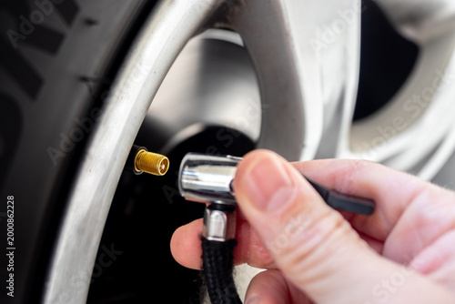 Close-up of a hand connecting an air pump to a car tire valve on an alloy wheel - concept of vehicle maintenance, tire inflation and safety check