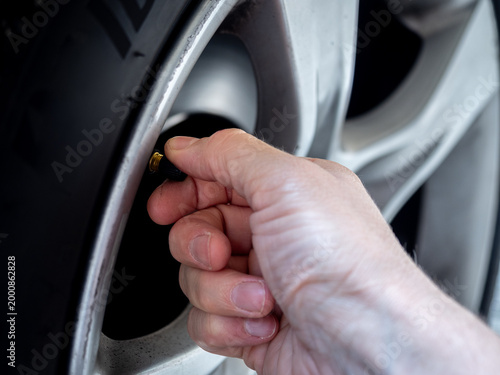 Close-up of a hand screwing a cap onto a car tire valve on an alloy wheel - concept of vehicle maintenance, tire inflation and safety check