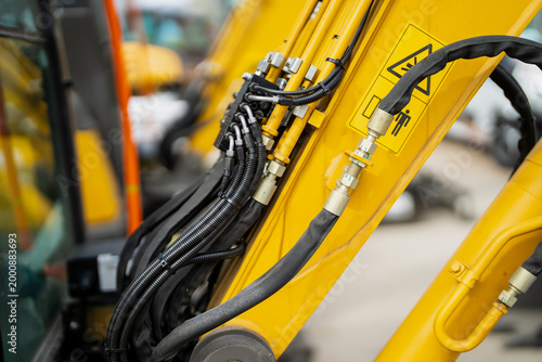 Excavator arm hydraulic hose routing with black protective sleeves, silver fittings and yellow boom for construction fleet service inspection work