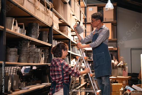 Canvastavla Pottery workshop with man and woman organizing metal bucket on shelf in warm stu