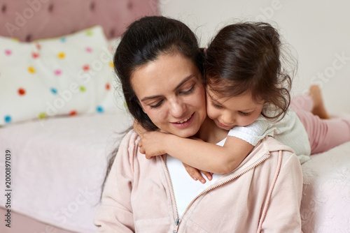 Mother and young child hugging in a close embrace. Expressing love, family bonding, and tenderness in a bedroom setting