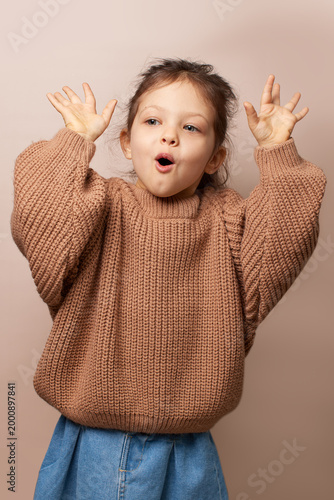 kid girl showing surprise and playful expression standing against beige background