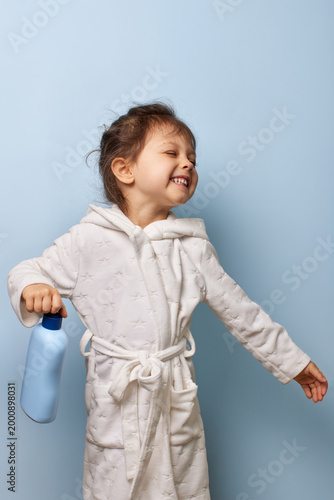 Young girl smiling with eyes closed after a bath, holding a skincare bottle