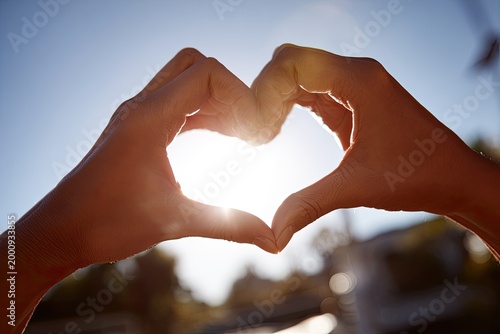 Two hands form a heart shape against a bright, sunlit sky, symbolizing love, connection, and positivity.