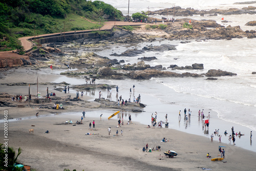High angle view of Sinquerim Candolim beach in Goa with people enjoying shoreline, rocky coast, and waves during a busy day.