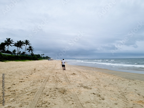 Man in patterned shirt standing on an empty beach with monsoon clouds waves on the side and trees showing lack of tourism in Goa