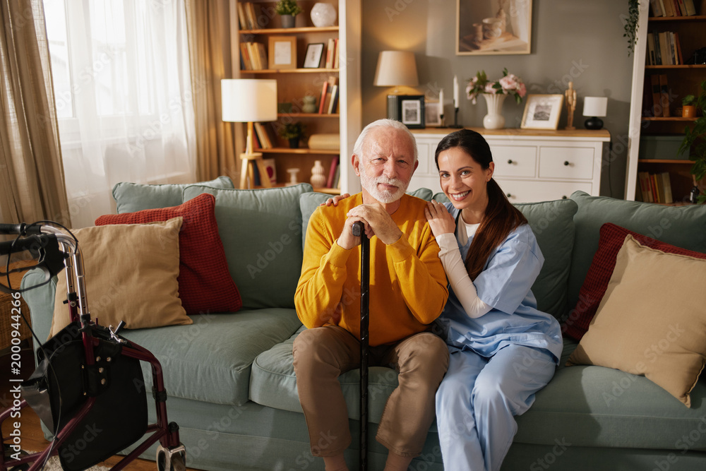 Obraz premium A home health nurse smiles as she sits next to an elderly man in a living room. They are enjoying each other's company while the nurse offers support.