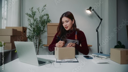 Young entrepreneur writing address on a cardboard box for shipping in her online store office for a small business