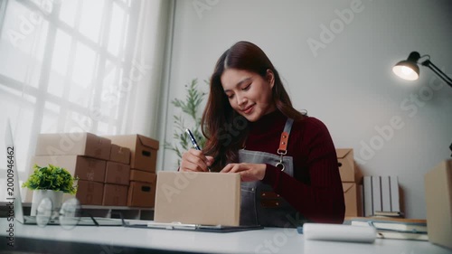 Small business owner writing customer address on a cardboard box for shipping in her home office, preparing online orders