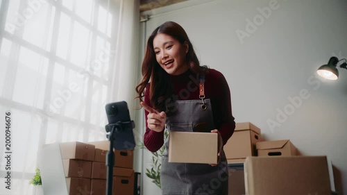 Asian entrepreneur livestreaming and selling products online with her smartphone in her home office