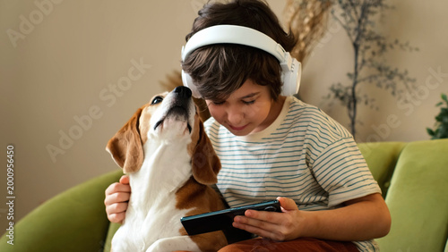 A boy rests cheek to cheek with a beagle on a green sofa while listening through headphones and holding a phone. Family pets and digital habits create peaceful moments of comfort and affection.