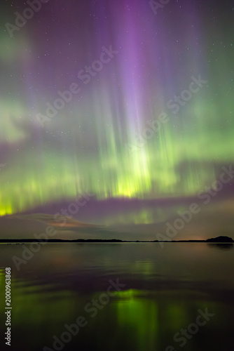 Anazing aurora borealis in the starry sky dancing over calm lake