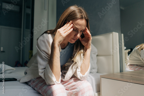Canvastavla A middle-aged woman sitting at home holds her hands on her temples