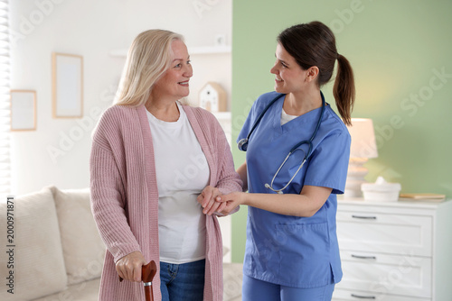 Foto Smiling care worker supporting senior woman with walking cane at nursing home