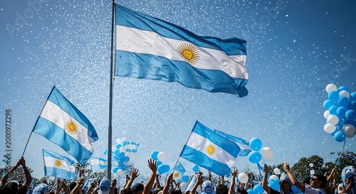 Argentina flag waving in the wind with a crowd of people cheering and blue balloons against a clear blue sky on a sunny day
