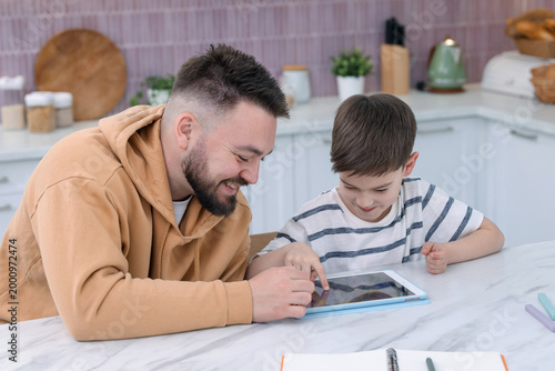 Father and his son using tablet at white table indoors