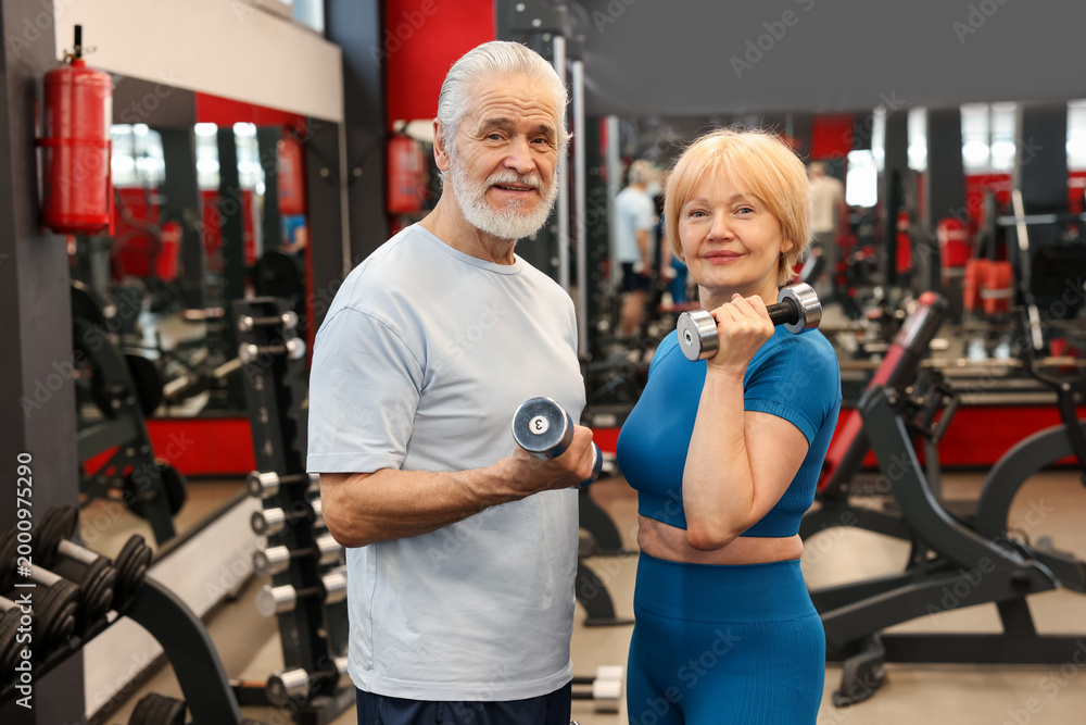 Fototapeta premium Senior couple training with dumbbells in gym