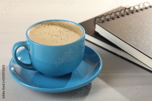 Cup of refreshing coffee and notebooks on light grey wooden table, closeup