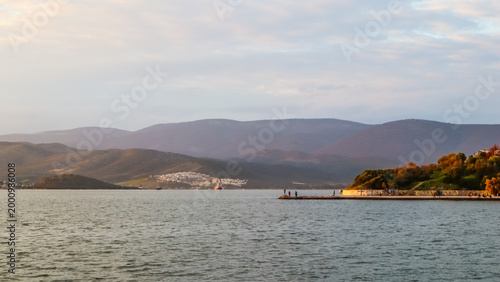 Foto Gulluk bay seascape with people fishing on a pier, coastal town and mountains in