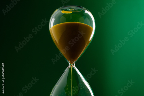 A green hourglass counting down against a green background, representing the concept of working with time and using time most efficiently.