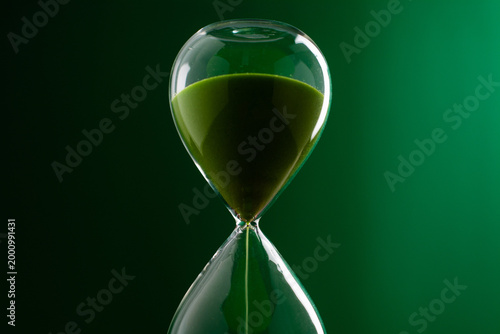 A green hourglass counting down against a green background, representing the concept of working with time and using time most efficiently.