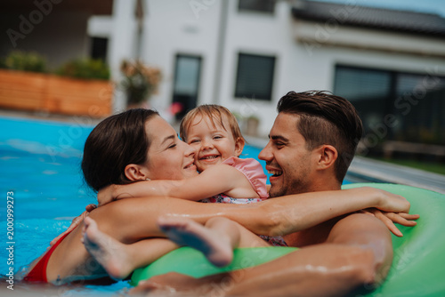 Fotografi Parents and child having fun with floatie in garden swimming pool